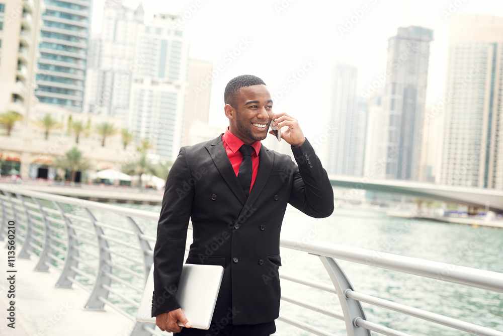 Businessman walking with laptop and talking on smart phone at Dubai Marina. Businessman walking with laptop and talking on smart phone at Dubai Marina.