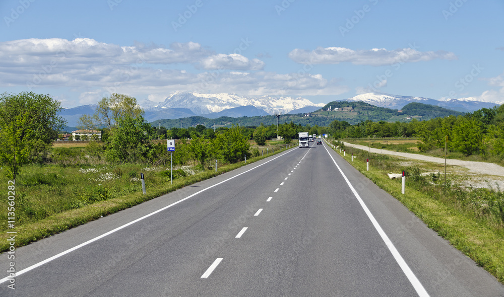 Gerade Autostraße mit verschneiten Bergen im Hintergrund Gerade Autostraße mit verschneiten Bergen im Hintergrund