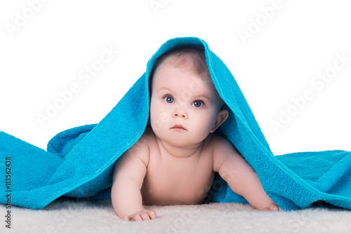 cute baby child with big eyes under blue towel on white, isolated. baby lying on a soft blanket, look up and tries to crawl on his belly