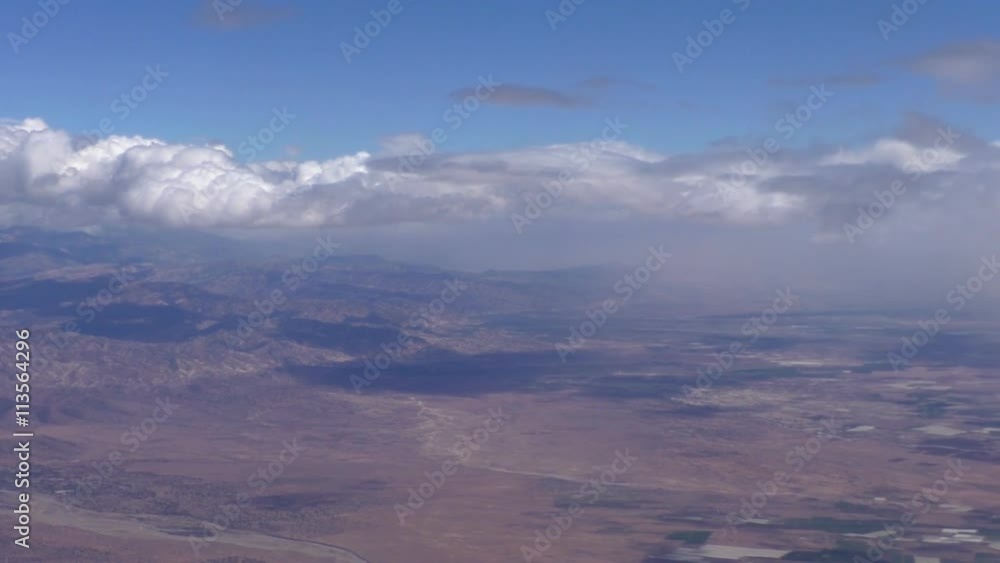 Aircraft passenger window view of High Atlas mountains in North Africa.Dry riverbed seen going down from mountains, white patches are agricultural greenhouses for fruits and vegetables.Bird's eye view Aircraft passenger window view of High Atlas mountains in North Africa.Dry riverbed seen going down from mountains, white patches are agricultural greenhouses for fruits and vegetables.Bird's eye view