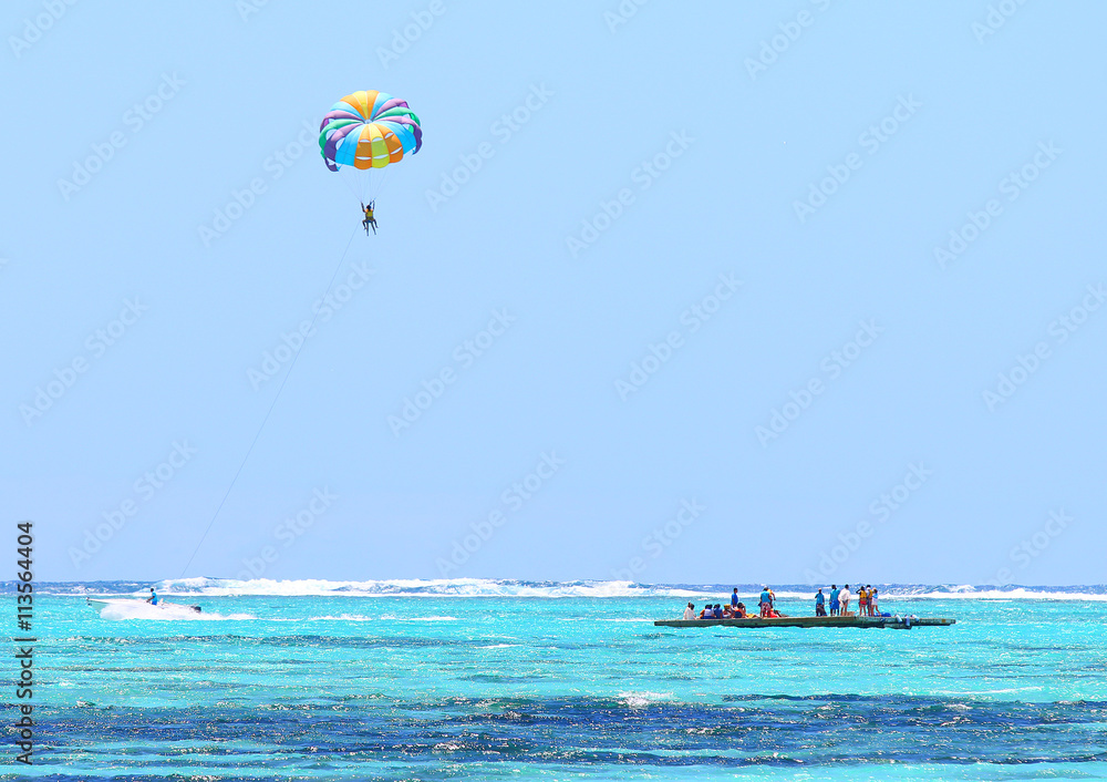 Parasailing over Indian Ocean near Mauritius Island. Summer on the beach. Outdoor sports and activities. Parasailing over Indian Ocean near Mauritius Island. Summer on the beach. Outdoor sports and activities.