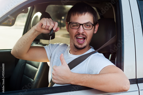 Young male caucasian driver is holding new car key and showing thumb up