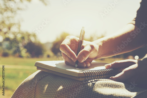 girls hands with pen writing on notebook in park