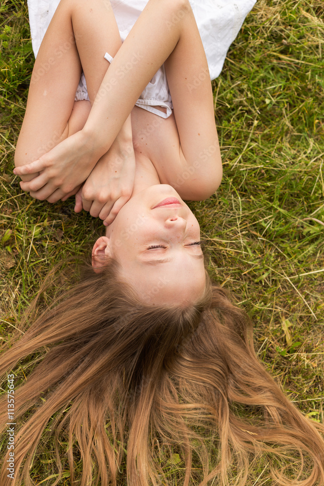 Portrait of a beautiful young girl lying on the grass outdoors in summer Portrait of a beautiful young girl lying on the grass outdoors in summer