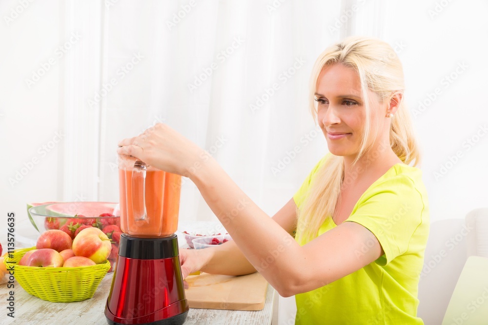 A beautiful mature woman preparing a smoothie or juice with fruits in the kitchen.. A beautiful mature woman preparing a smoothie or juice with fruits in the kitchen..