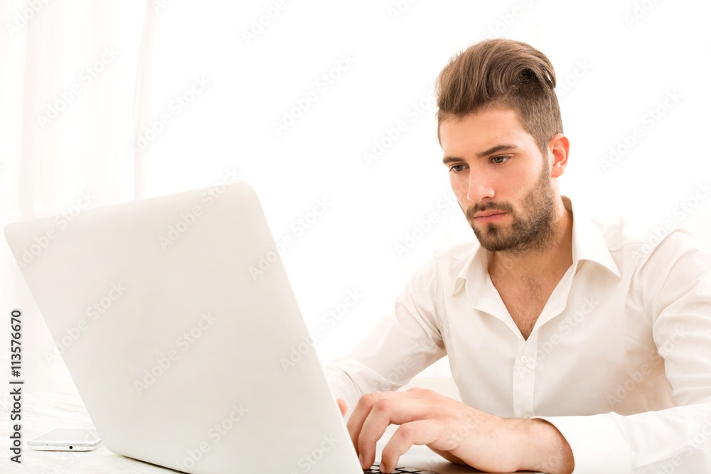 Attractive young man sitting at the table with a laptop computer.. Attractive young man sitting at the table with a laptop computer..