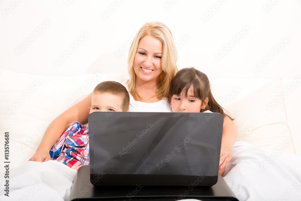 A mother using with her son and daughter a laptop computer in bed.. A mother using with her son and daughter a laptop computer in bed..