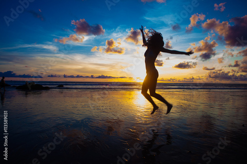sunset silhouette of young fit woman jumping at beach