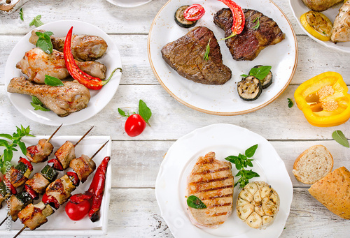 Assorted grilled meats and vegetables on a white wooden table.