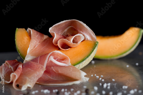 Jambon mix. Ham. Traditional Italian and Spanish salting, smoking, dry-cured dish - jamon Serrano and prosciutto crudo sliced with melon on grey background. Copy space. Closeup. 