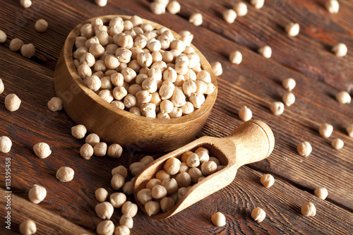 Chickpeas in bowl and scoop on wooden table