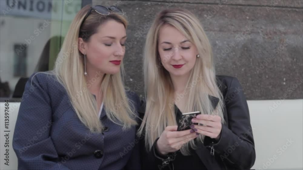 Two blondes are sitting in a café and discuss photos in the smartphone Two blondes are sitting in a café and discuss photos in the smartphone