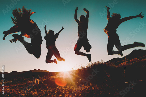 Four people jumping over the sky at sunset. Sunbeam in the background. photo