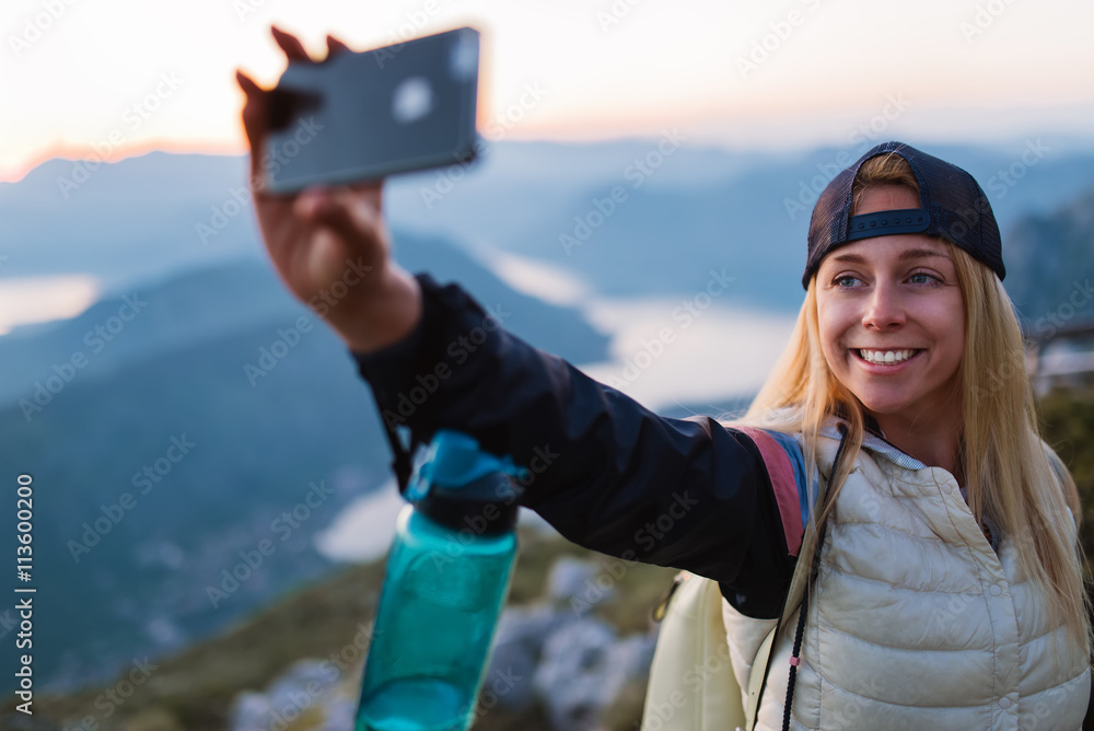 Shot of a young female tourist taking a selfie while standing on top of a mountain