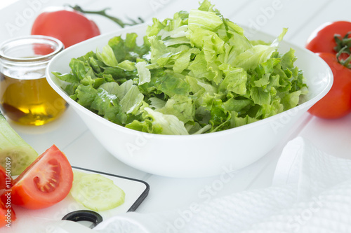 Preparing a healthy fresh salad with tomato, lettuce, cucumber and oil
