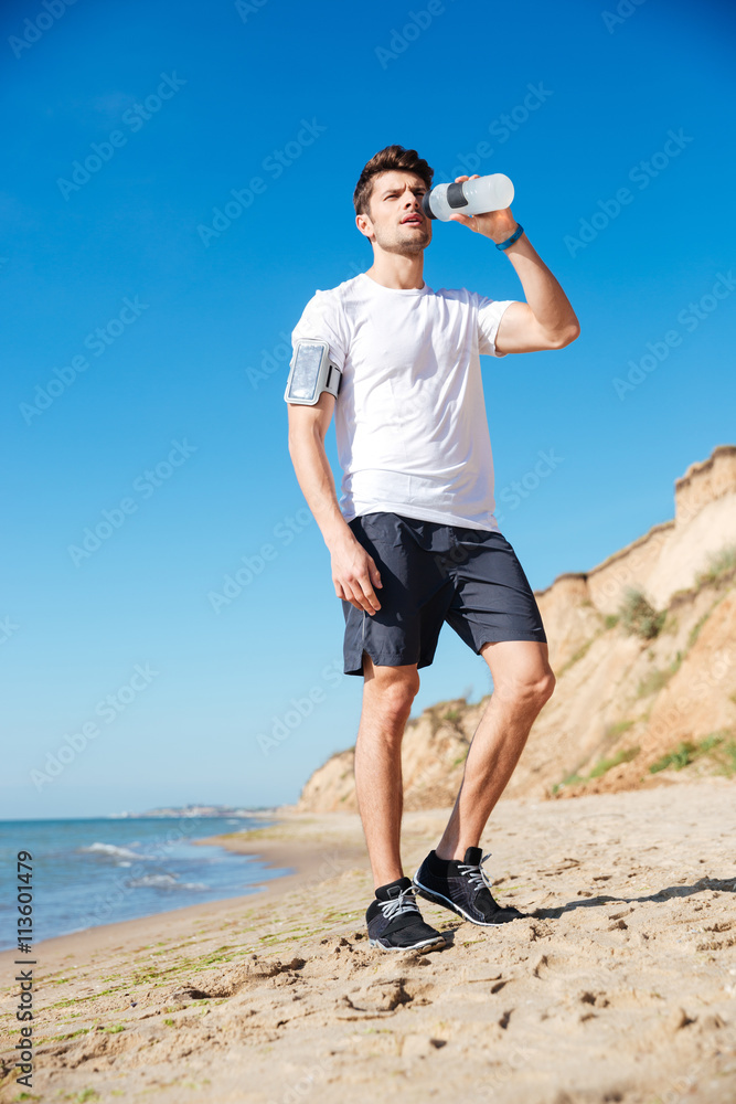 Sportsman standing and drinking water on the beach Sportsman standing and drinking water on the beach