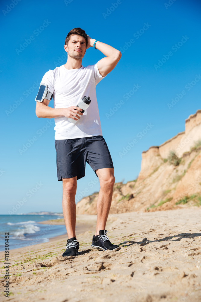 Attractive young sportsman with bottle of water on the beach