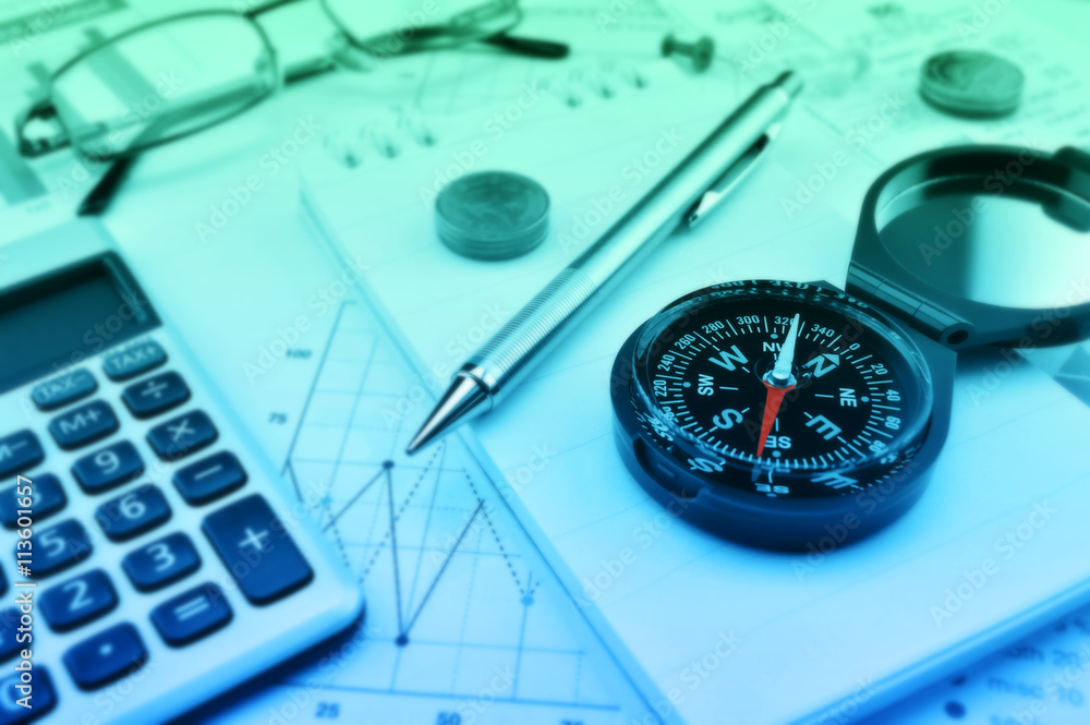 Compass, pen and coin on notebook, accounting background Compass, pen and coin on notebook, accounting background