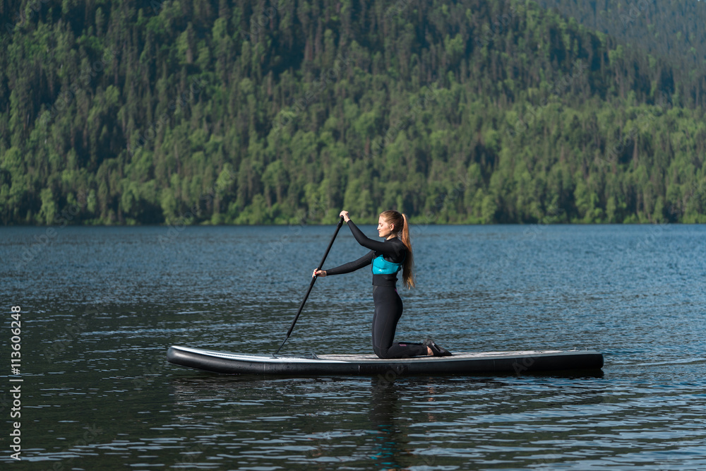 woman in black wetsuit paddeling at calm altai lake teletskoe
