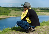 lonely boy teenager sits on a hill above lake