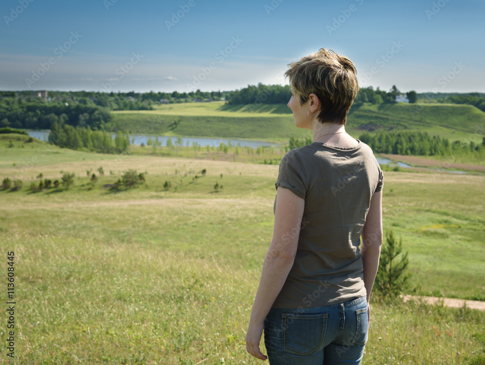 lonely woman standing with her back on green field