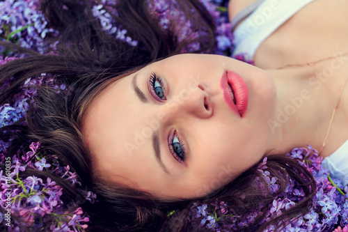 Young beautiful girl lies on the lilac flowers.
