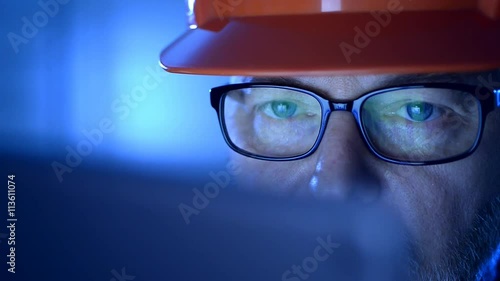 Blue ambiance, a engineer with a security helmet  working on a laptop. 