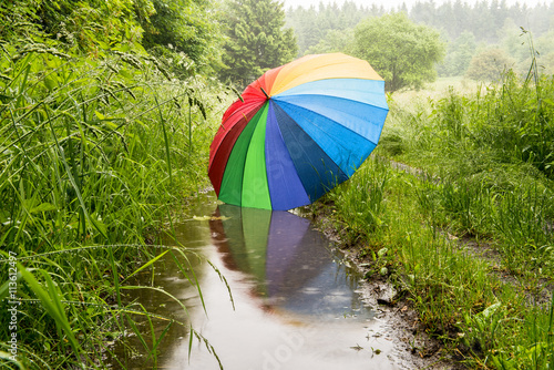 großer bunter Regenschirm spiegelt sich in einer Pfütze