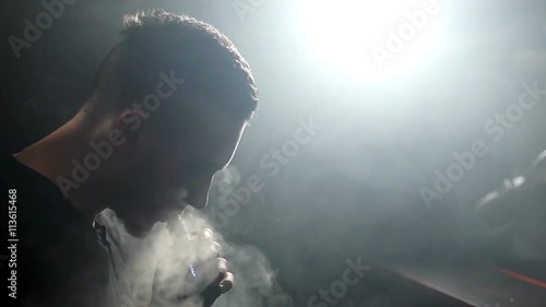 young vaper man exhaling big clouds of smoke with e-cigarette vape in slowmotion photo