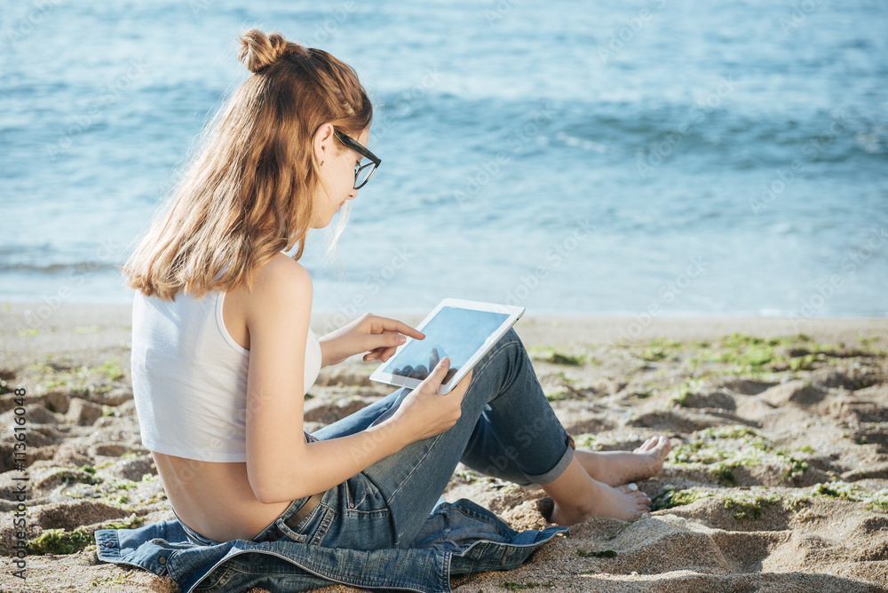 Girl using a digital tablet by the sea. 