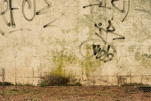 Hintergrund – Schmutzige Wand mit Graffit Schmierereien und Ascheplatz mit Unkraut als Boden