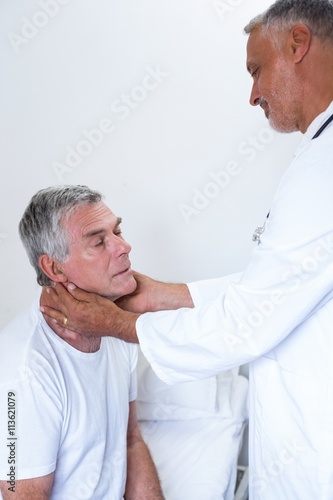 Male doctor examining senior mans neck