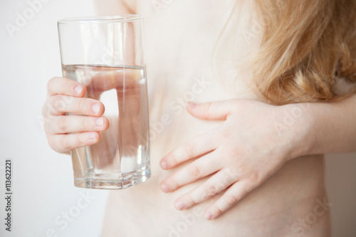 Little girl holding a glass of water and touching her tummy