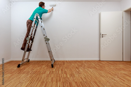 Mann auf Leiter beim Streichen der Wand