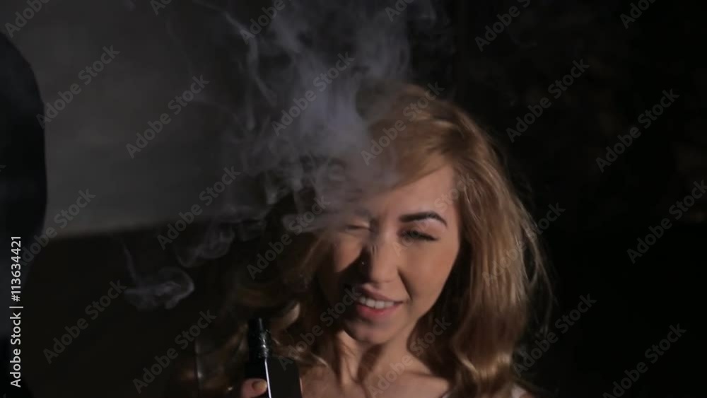 Woman smoke vaporizer or electronic cigarette, smile and wink. Female with good mood recline Woman smoke vaporizer or electronic cigarette, smile and wink. Female with good mood recline