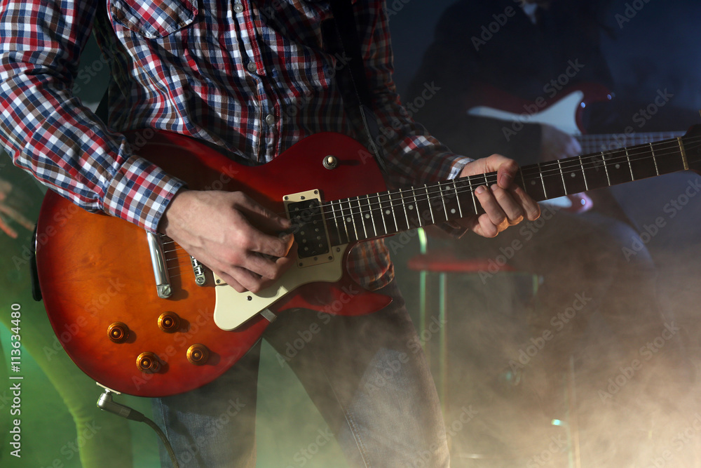 Obraz premium Young man playing electric guitar on lighted foggy background