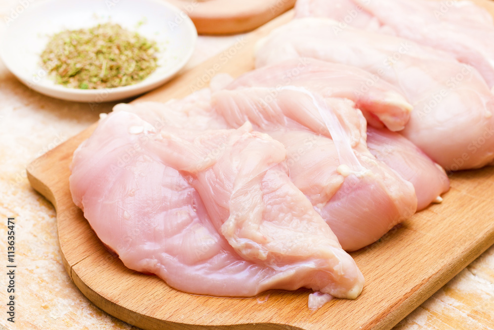 Close-up of chicken on wooden board on the kitchen table. In the background is plate with spices and chopped onion Close-up of chicken on wooden board on the kitchen table. In the background is plate with spices and chopped onion