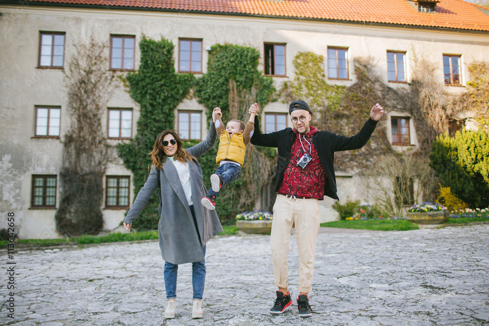 Happy young family, father and mother keep son's hands outdoors