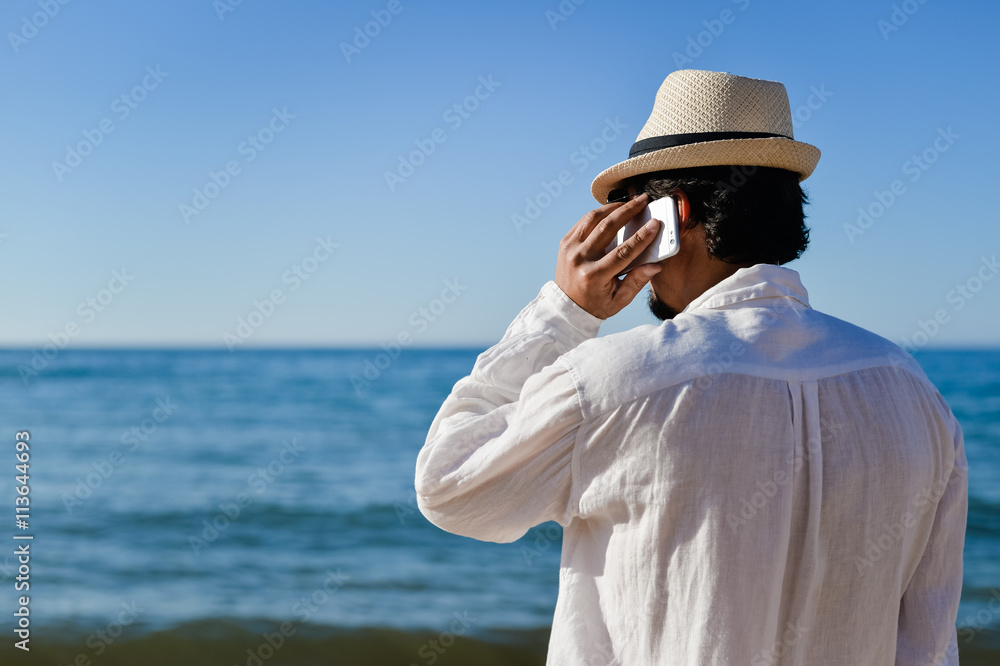 Back side view of man talking on smart phone, background vacation beach