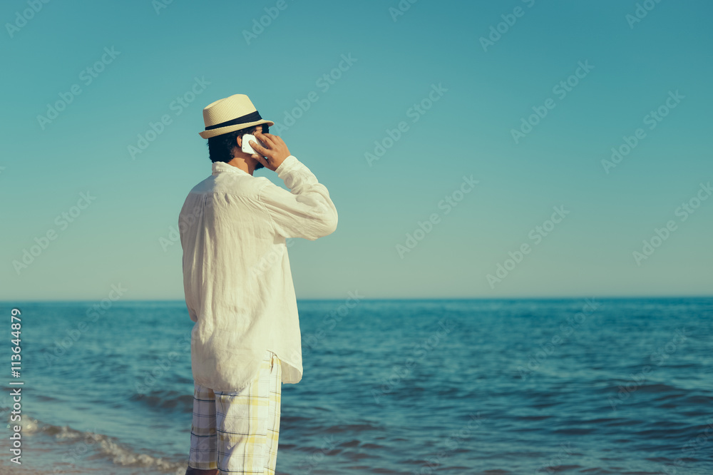 Back view of man talking holding mobile phone, blue sky sea outdoors background