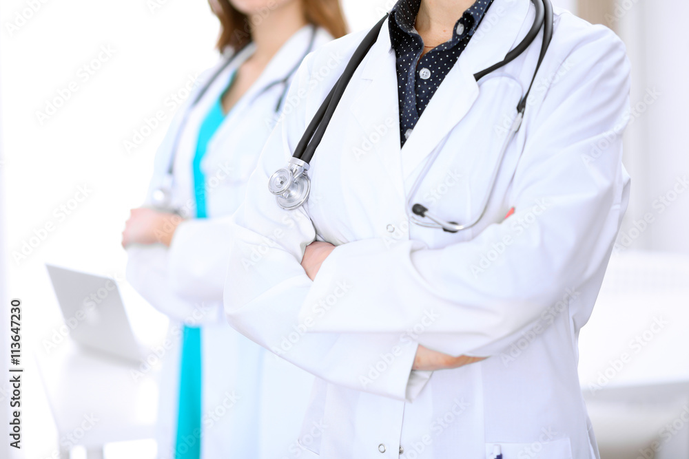Close up of unknown female doctor standing in a hospital with her colleague in the background Close up of unknown female doctor standing in a hospital with her colleague in the background