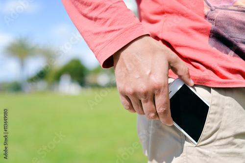 Closeup man taking smartphone from pocket on sunny outdoors background