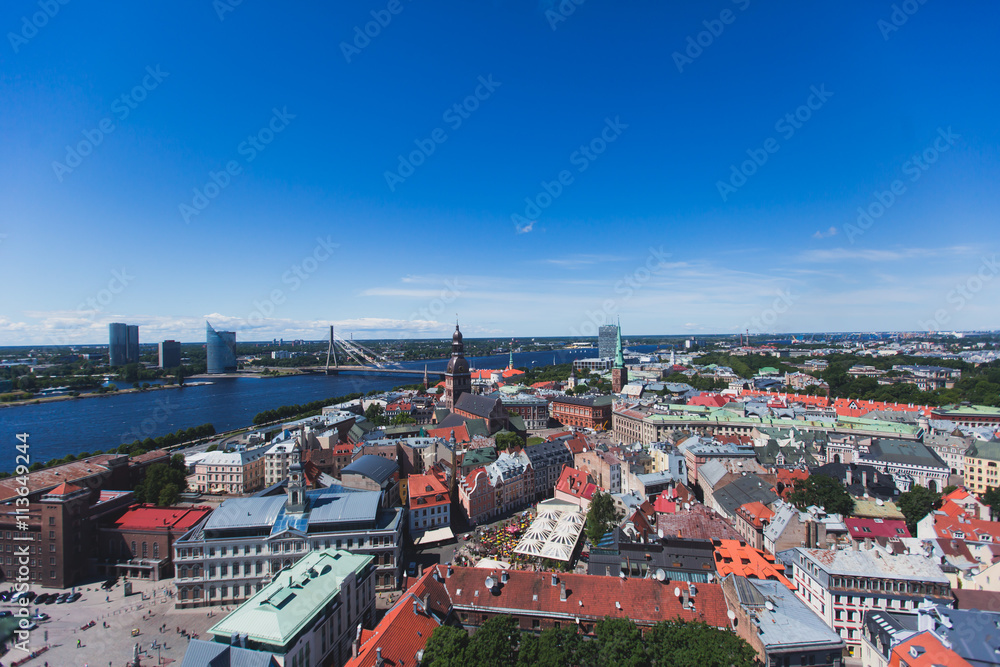 Obraz premium Beautiful super wide-angle panoramic aerial view of Riga, Latvia with harbor and skyline with scenery beyond the city, seen from the St. Peters Church observation tower, sunny summer day