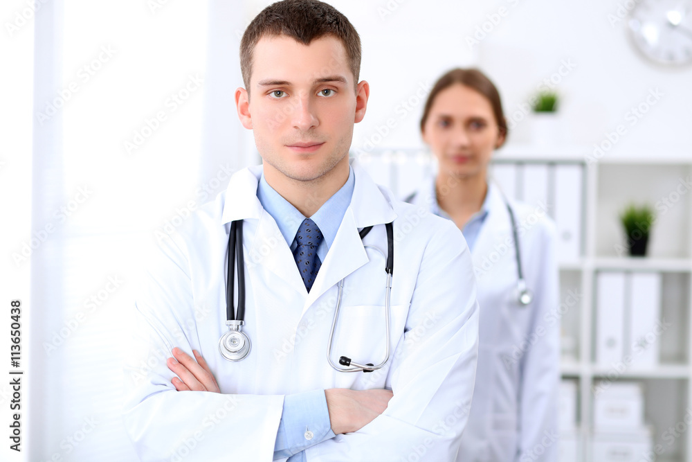 Friendly male doctor on the background of female doctor in hospital office. Ready to examine and help patients. High level and quality medical service concept. Best treatment and patient care concept