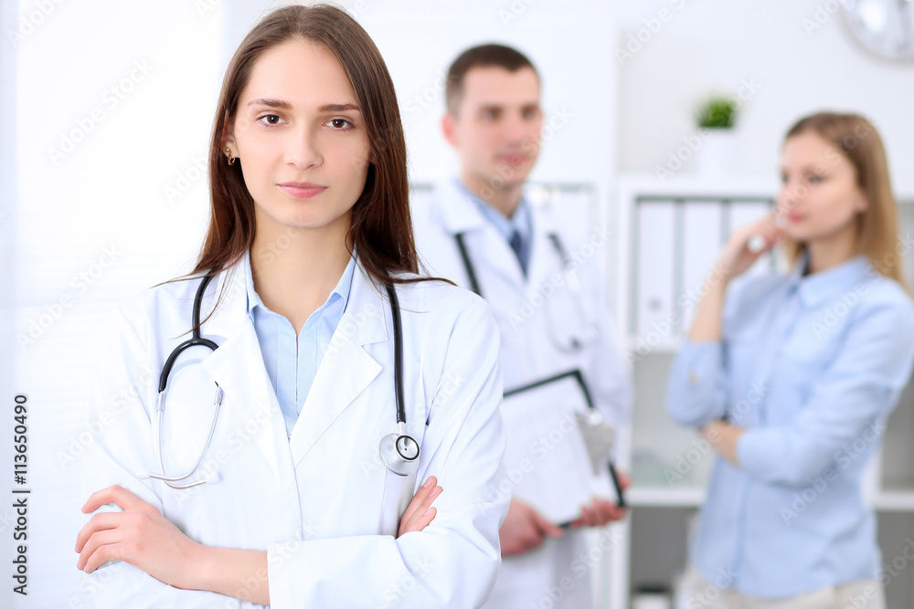 Young beautiful female doctor smiling on the background with patient and his doctor in hospital. High level and quality medical service concept. Young beautiful female doctor smiling on the background with patient and his doctor in hospital. High level and quality medical service concept.