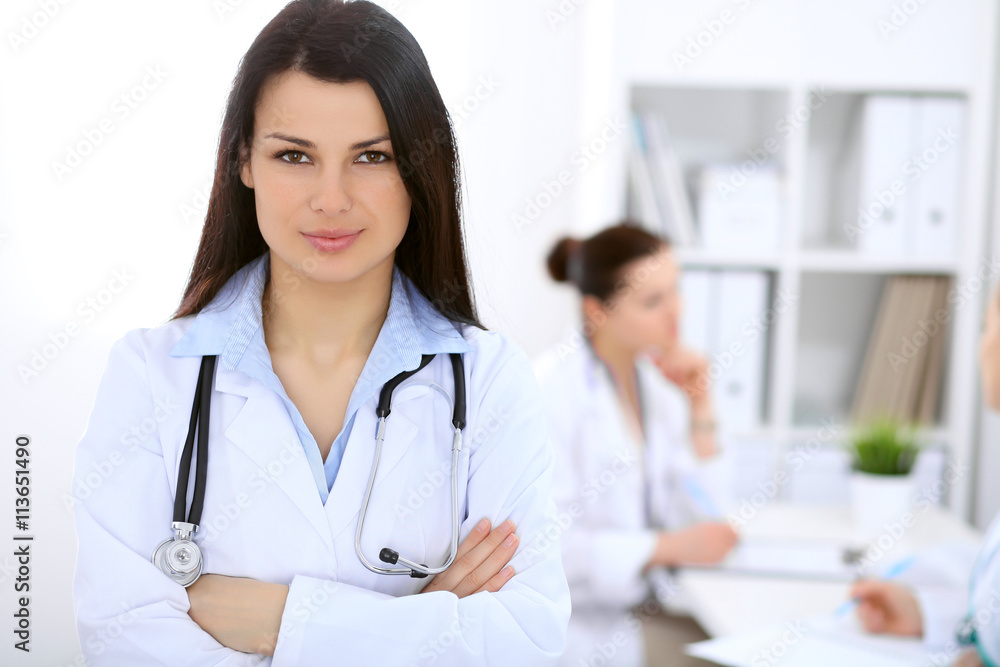 Brunette female doctor on the background of colleagues talking to each other in hospital Brunette female doctor on the background of colleagues talking to each other in hospital