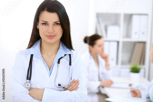 Brunette female doctor on the background of colleagues talking to each other in hospital