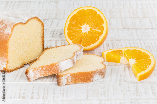Orangensandkuchen, angeschnitten mit geschnittener Orange auf weisser Holzplatte,