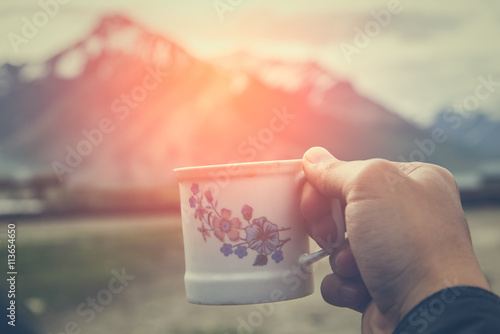 Hand holding a cup of masala chia tea with warm light and Himala
