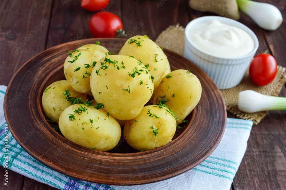 Young boiled potatoes with butter and dill in a clay bowl on a wooden background. Close up